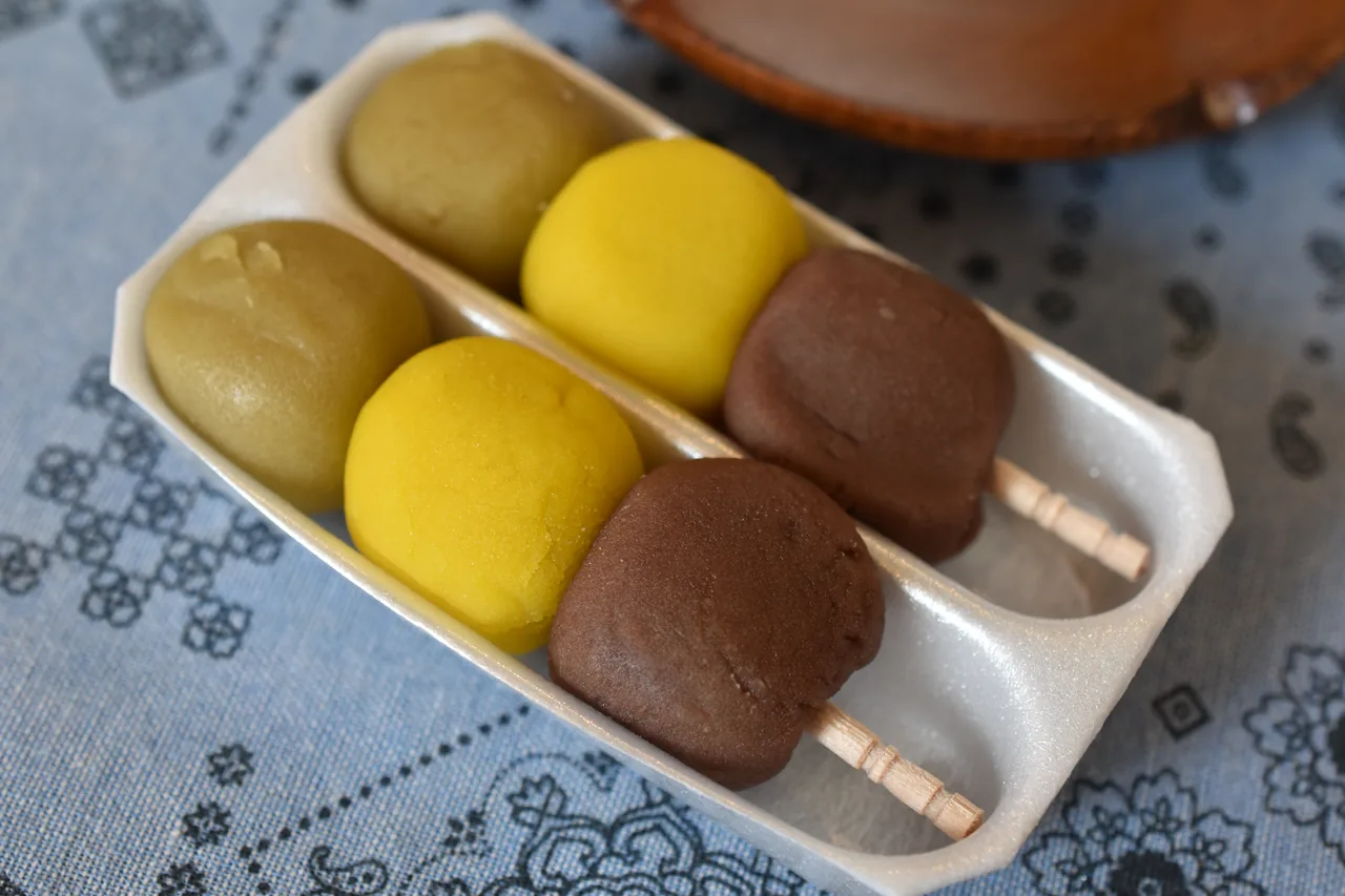 A plate with two skewers of green, yellow and red-bean dumplings