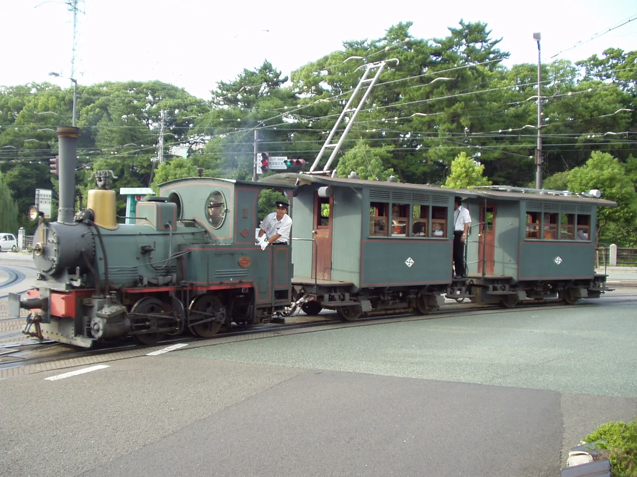 The Botchan Train, a black steam-style engine pulling two green carriages, running on street tracks