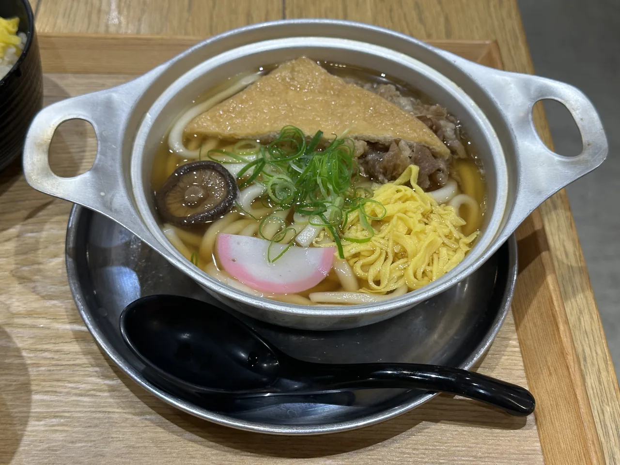 Nabeyaki udon in an aluminium pot with fried tofu, fish cake, shiitake and egg