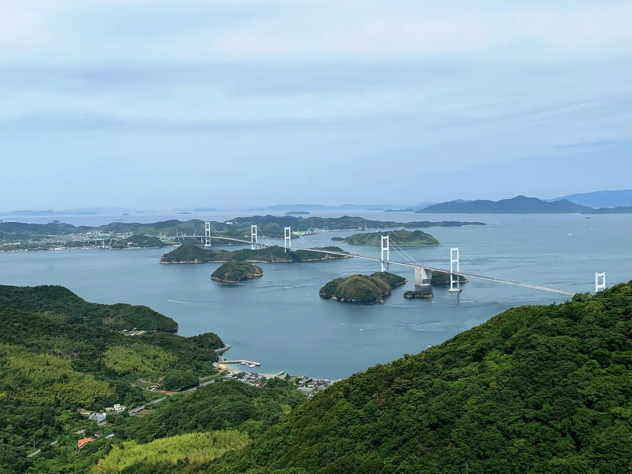 The Kurushima-Kaikyo Bridge, three suspension spans in a row, over a sea dotted with islands, seen from a high lookout