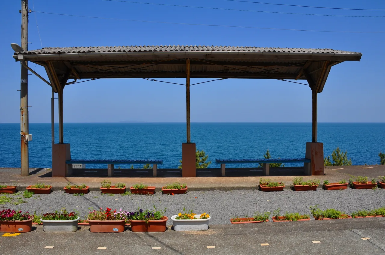 Shimonada Station's platform roof and bench, with blue sea stretching to the horizon