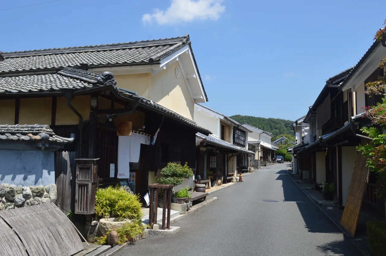 Uchiko's Yokaichi street on a clear day, tiled-roof shops and white plaster houses along a slope, empty